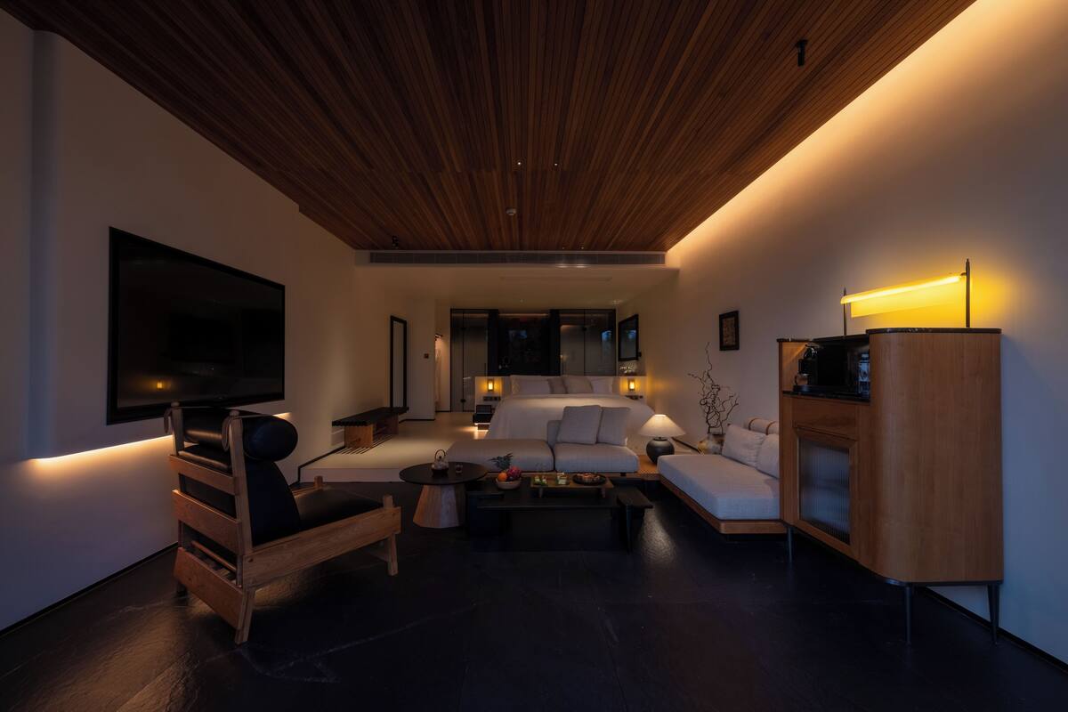 A modern living room with a wooden ceiling, a large flat-screen TV, a sofa, a coffee table, and a cabinet.