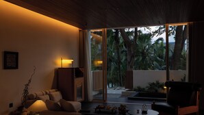 A modern living room with a sofa, a coffee table, and a chair. There is a lamp on the table and a plant on the floor. - Anlai Rainforest Luxury Resort (Xishuangbanna Dai)