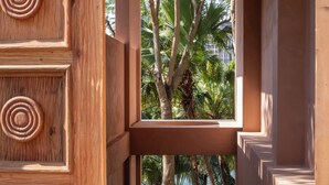 A wooden corridor with circular patterns, leading to a balcony with palm trees and a view of the sea. - Anlai Rainforest Luxury Resort (Xishuangbanna Dai)