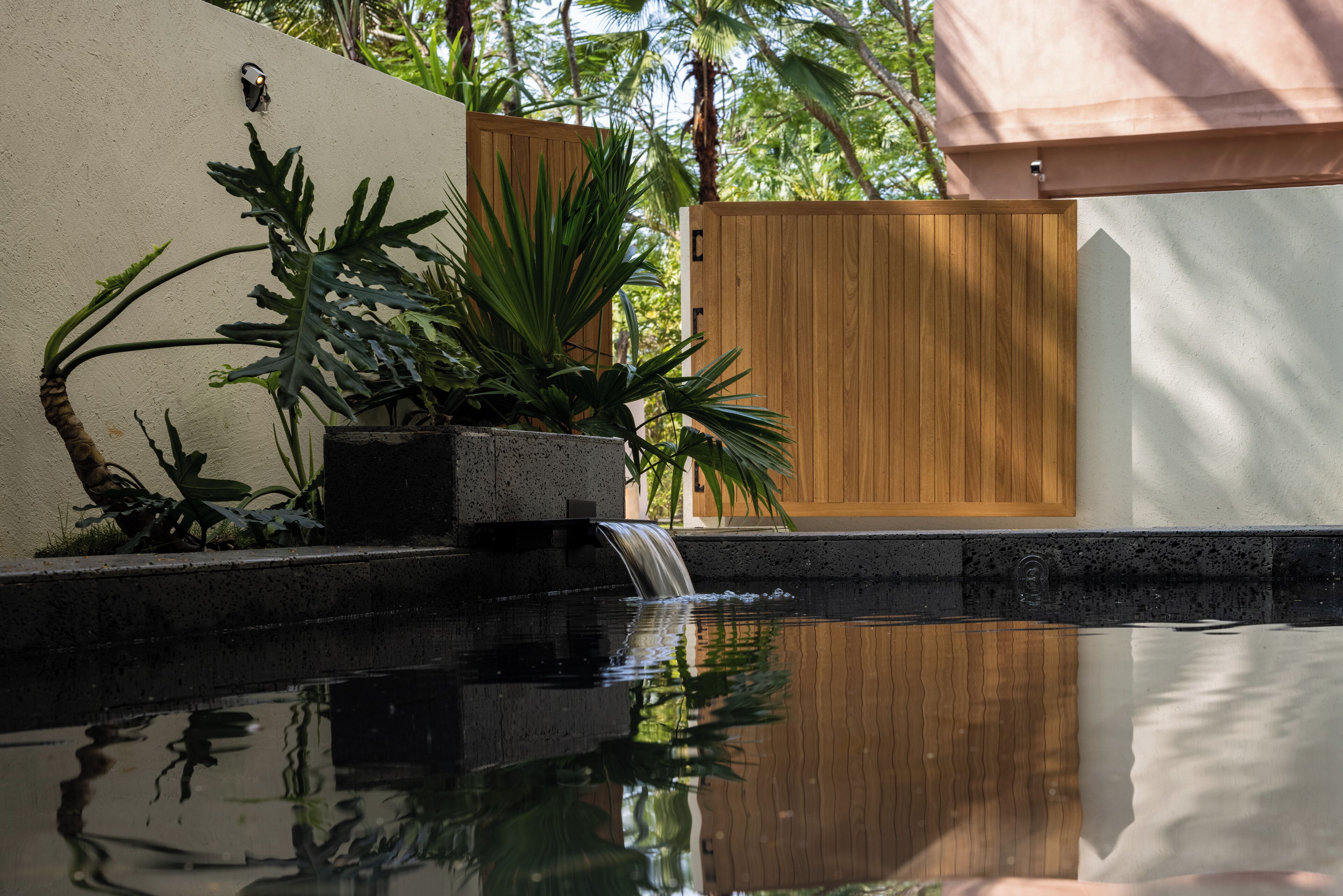 Un espace piscine paisible, agrémenté d’une clôture en bois, d’une végétation luxuriante et d’une petite cascade.
