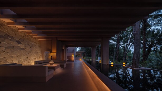 A modern, dimly lit corridor with a stone wall on one side and a wooden ceiling. - Anlai Rainforest Luxury Resort (Xishuangbanna Dai)