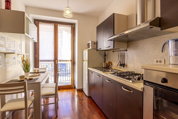 A modern kitchen with a gas stove, oven, and microwave, a dining area with a table and chairs, and a view through a glass door to an outdoor balcony. - GuestHost - A few steps from the historic center of Como, in an area well served and well connected by public transport, this space offers easy access to all the local attractions.Located on the second floor with elevator of a modern building, this 50 sq (Como)
