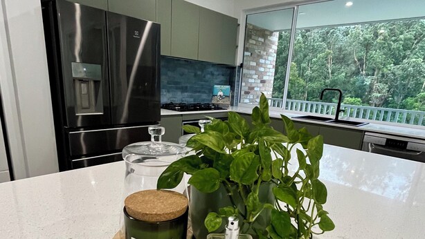 Une cuisine moderne dotée d’une grande fenêtre, d’un réfrigérateur, d’une cuisinière et d’un plan de travail agrémenté d’une plante, d’une bougie et d’une bouteille.