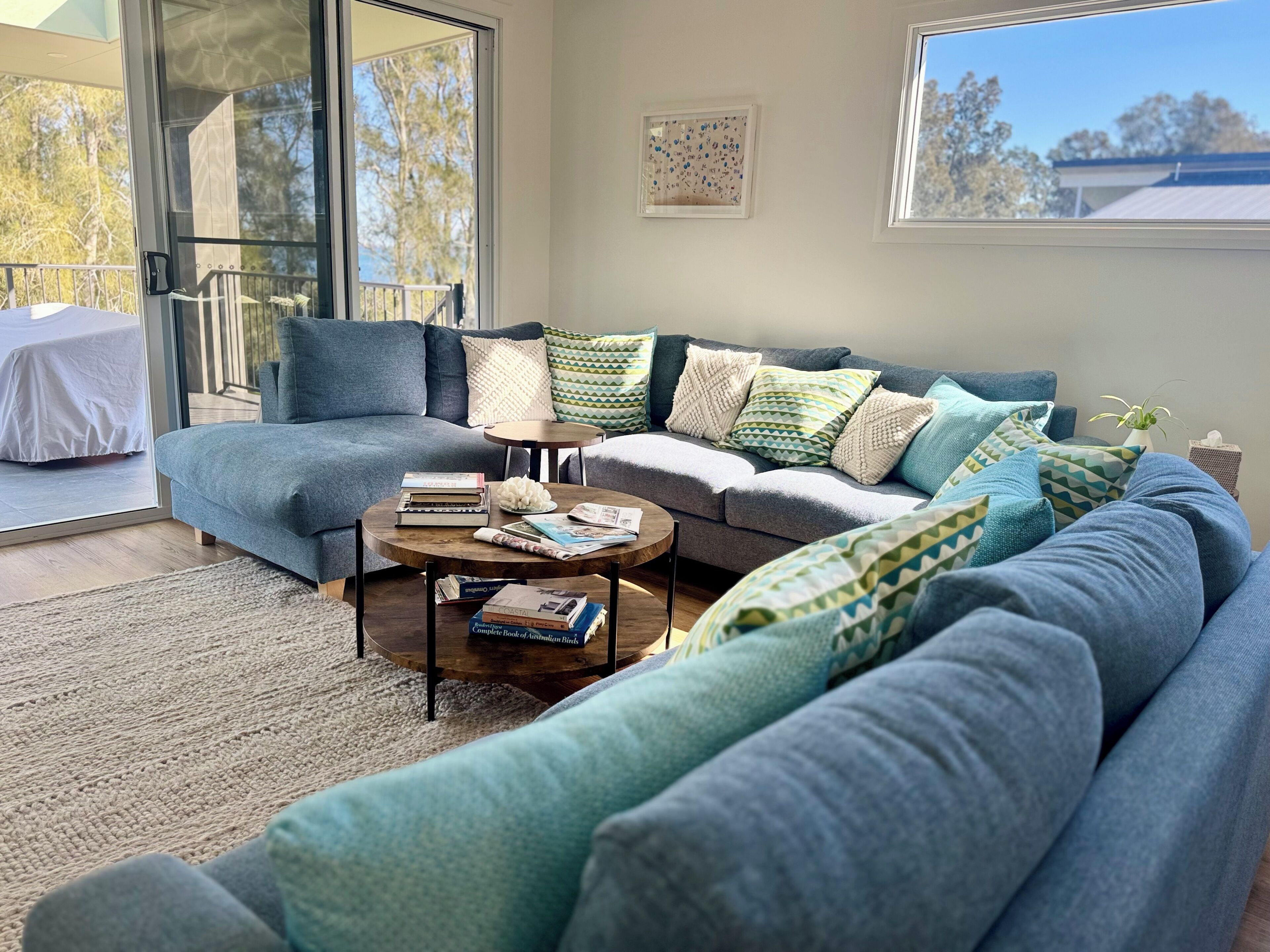 A modern living room with a grey sectional sofa, a coffee table, and a glass door leading to an outdoor balcony.