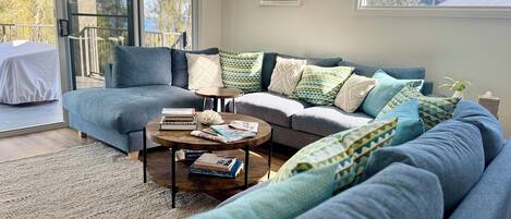 A modern living room with a grey sectional sofa, a coffee table, and a glass door leading to an outdoor balcony.