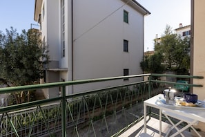 A balcony with a table, railing, and a view of a building and trees.