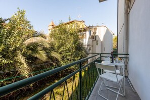 Un balcon avec une table et des chaises, entouré de verdure, et un bâtiment avec un toit en forme de dôme en arrière-plan.