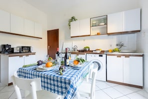 A compact kitchen with white cabinets, a dining table with a blue checkered tablecloth, and a washing machine.