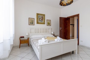 A bedroom with a bed, bedside tables, a wooden door, and a tiled floor.