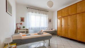 Un dormitorio con dos camas, un escritorio, una silla, un armario y una ventana con cortinas.