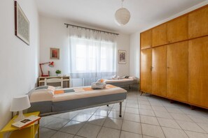Una camera da letto con due letti, una scrivania, una sedia, un armadio e una finestra con tende.