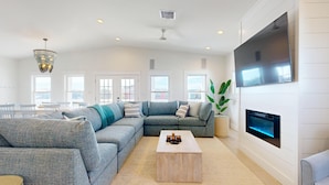 A modern living room with a sectional sofa, a coffee table, a flat-screen TV mounted on the wall, and a fireplace. - PP627 Private Heated Pool, Golf Cart Included, Parking for 6 (Port Aransas)