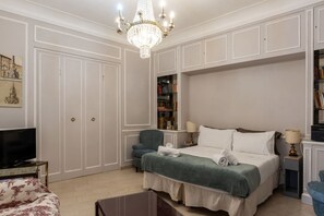 A bedroom with a bed, a television, a bookshelf, and a chandelier.
