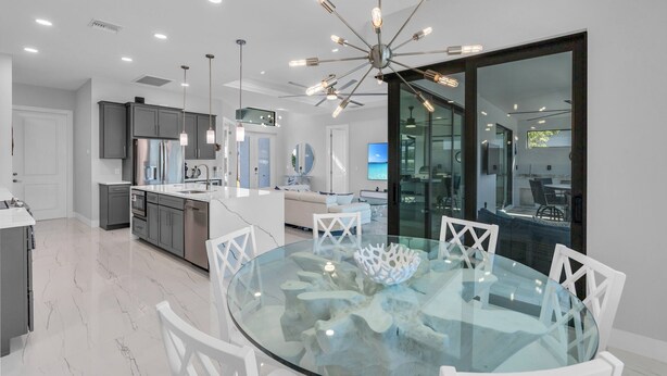 Una cocina moderna con una isla central, armarios blancos y una mesa de comedor de cristal con sillas blancas.
