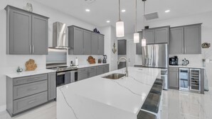 Una cocina moderna con armarios grises, encimeras de mármol blanco, electrodomésticos de acero inoxidable e iluminación colgante.