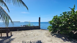 Una playa arenosa con un banco, una estructura de concreto y vista al mar.