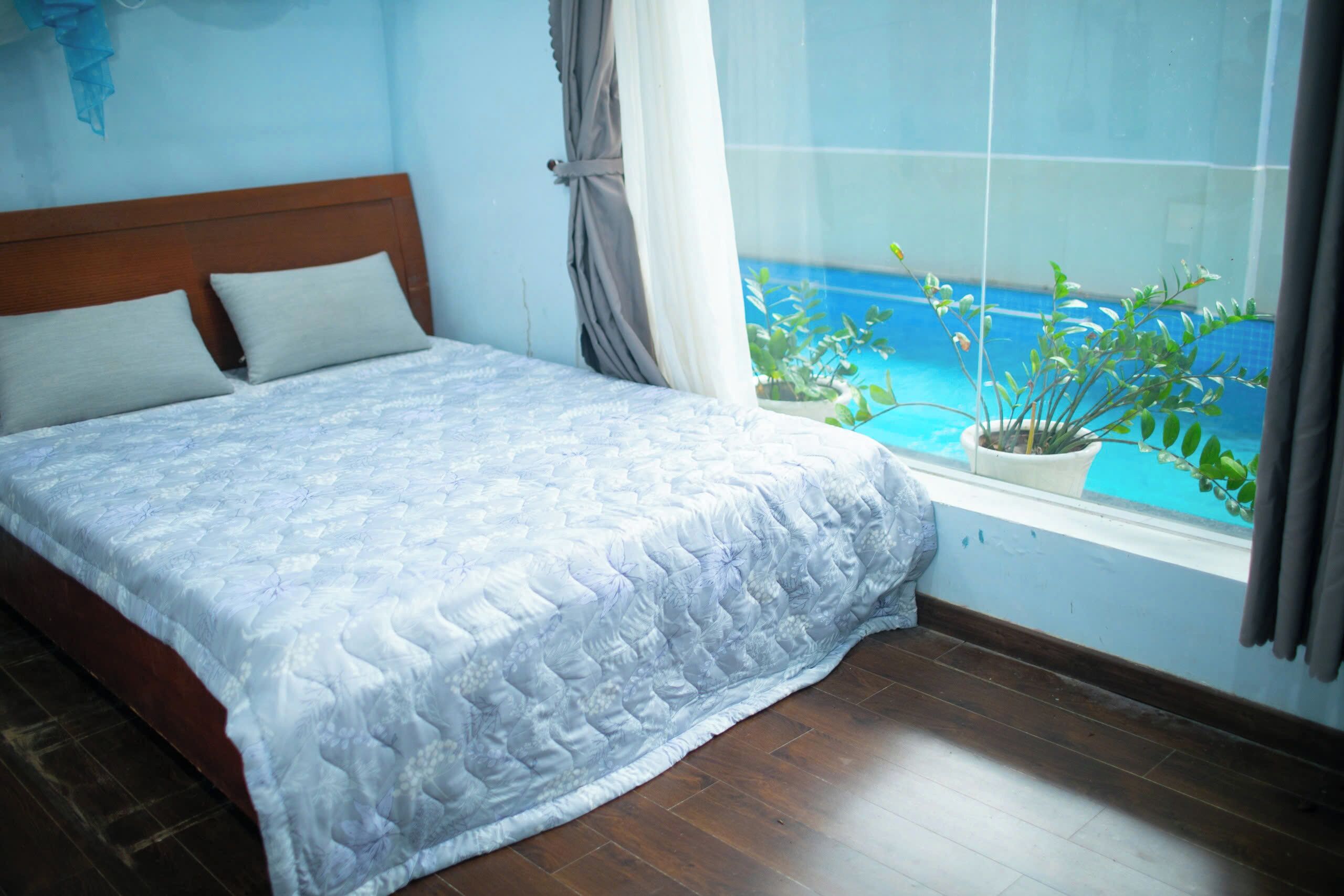 A bedroom with a bed, a window with a view of the sea, and a potted plant on the windowsill.