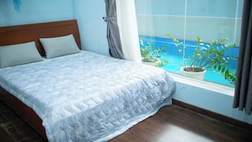 A bedroom with a bed, a window with a view of the sea, and a potted plant on the windowsill.