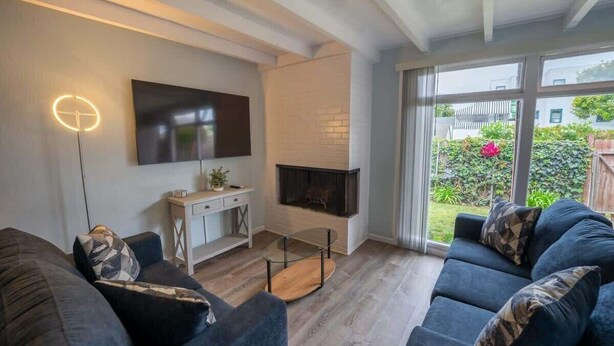 Ein modernes Wohnzimmer mit Flachbildfernseher, Kamin und großem Fenster mit Blick auf den Garten.