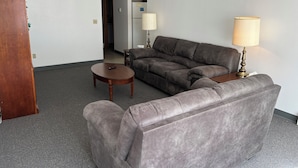A living room with a grey sofa, a small round table, and two lamps. - Adak Island Inn (Adak Island)