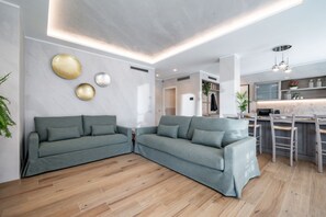 A modern living room with a grey sectional sofa, wooden flooring, and a kitchen area with a bar. - Villa Sunrise with pool and large private garden - few step from the beach  (Dervio)