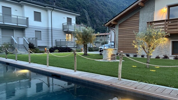 A pool area with a wooden deck, a grassy lawn, and a mountain backdrop. - Villa Sunrise with pool and large private garden - few step from the beach  (Dervio)
