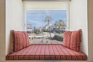 Un siège de fenêtre avec des coussins à rayures et une vue sur les bâtiments et les arbres.