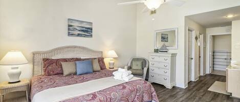 A bedroom with a bed, two bedside lamps, a ceiling fan, a chair, a dresser, and a mirror.
