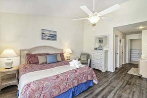 Une chambre à coucher comprenant un lit, deux lampes de chevet, un ventilateur de plafond, une chaise, une commode et un miroir.