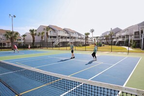 A tennis court with players, surrounded by residential buildings.