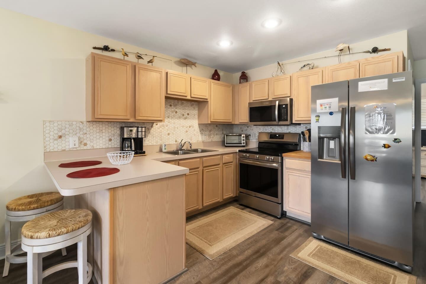 Una cocina compacta con armarios de madera, refrigerador de acero inoxidable, microondas, horno y lavamanos.