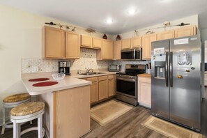 A compact kitchen with wooden cabinets, a stainless steel refrigerator, a microwave, an oven, and a sink.