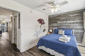 A bedroom with a bed, a ceiling fan, a wooden accent wall, and a door leading to a balcony.