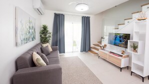 En moderne stue med en grå sofa, et fladskærms-tv, en trappe og en hvid reol.