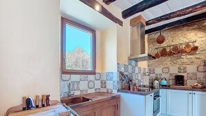A kitchen with a stone backsplash, wooden cabinets, a window, and hanging pots. - Vacation home Durand by Interhome (Saint Chamarand)