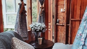 Ein gemütliches Blockhaus-Interieur mit Holzvertäfelung, einer Couch mit gemusterten Kissen, einem kleinen Tisch mit Blumentopf und zurückgebundenen Vorhängen an den Fenstern.
