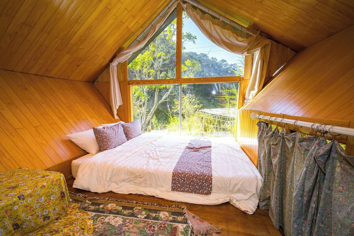 Quarto com uma grande janela, teto de madeira e cama com roupa de cama florida.