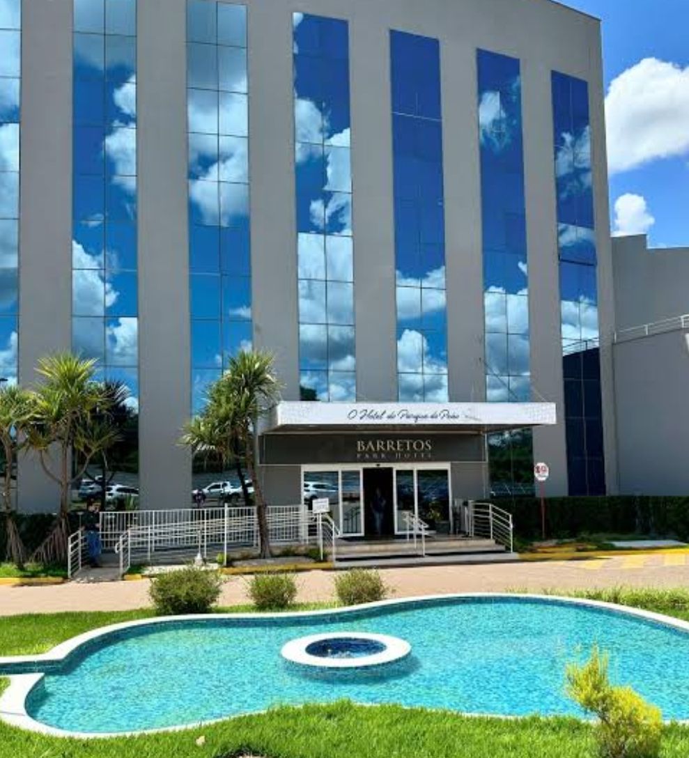 A hotel with a large reflective glass facade, a pool area, and a sign indicating it is a Barretos Park Hotel.