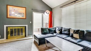 A modern living room with a sectional sofa, a fireplace, and a large window with blinds.