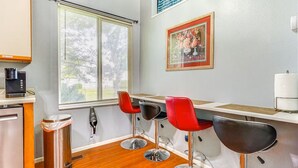 A kitchenette with a coffee machine, a trash can, and a window with blinds.