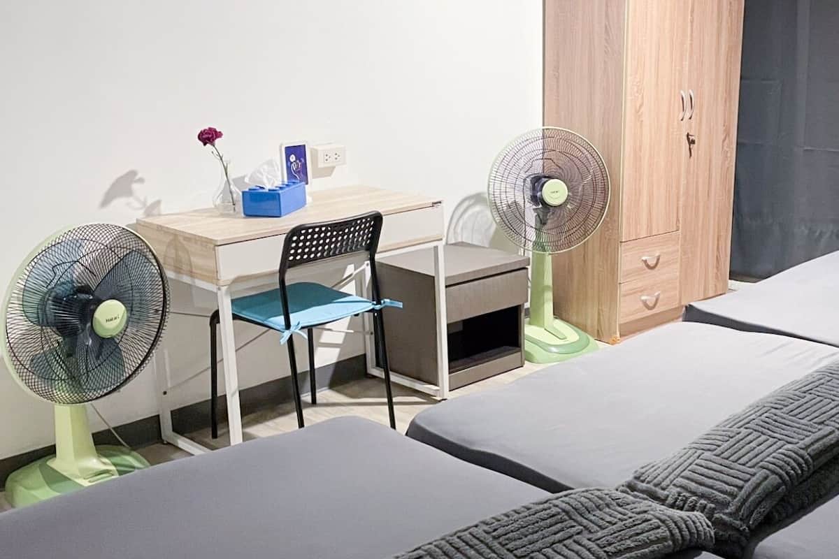 Une chambre d’hôtel équipée d’un bureau, de deux lits simples, d’une armoire et de deux ventilateurs sur pied.