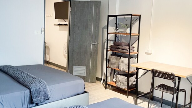A bedroom with a bed, a desk, and a shelving unit with towels. - MAXi MaMa Room (Bangkok)