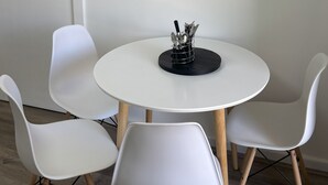 A dining area with a round white table, four white chairs, and a metal utensil holder. A framed picture of a beach scene hangs on the wall. - Peace and Joy (Para Hills)