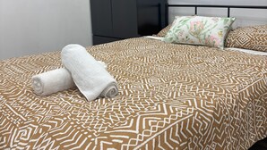 A neatly made bed with a patterned bedspread, a rolled white towel, and a floral pillow. - Peace and Joy (Para Hills)