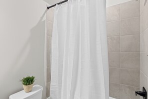 A bathroom with a white shower curtain, beige tiles, a potted plant, and a toilet.