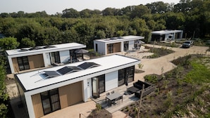 Una casa moderna de dos pisos con paneles solares, un patio y un automóvil estacionado cerca.