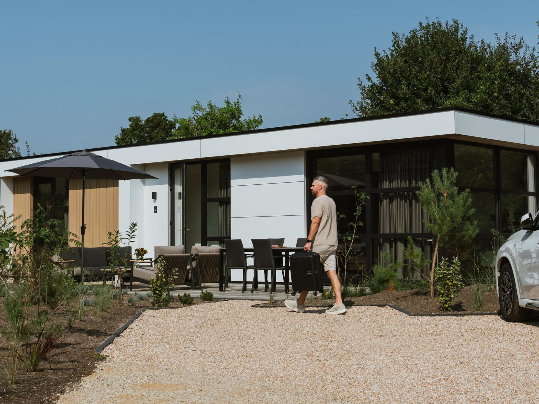 Une maison moderne dotée d’un patio, d’un espace salon extérieur et d’une voiture garée à proximité.