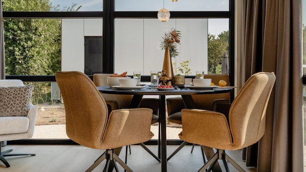 Un comedor moderno con una mesa redonda, cuatro sillas y un jarrón con flores secas.