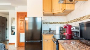 Una cocina moderna con armarios de madera, un refrigerador de acero inoxidable, una cafetera roja y un horno negro.