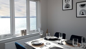 En matplats med ett bord dukat för fyra personer, utsikt över vattnet och en bro, samt inramade konstverk på väggen.